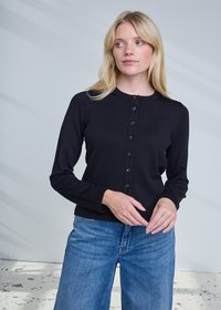 Cardigan nero a maniche lunghe con scollo rotondo, caratterizzato da una chiusura frontale con bottoni e design aderente. Abbinato a jeans azzurri.