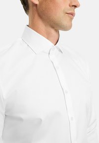 Weißes Hemd mit Button-Down-Kragen, glatter Textur und taillierter Passform, mit sichtbaren Knöpfen entlang der Frontblende.