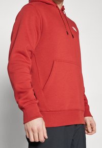 Rote Kapuzenjacke aus weichem Stoff, mit einer Fronttasche, gerippten Bündchen und Saum sowie verstellbarem Zugband an der Kapuze.