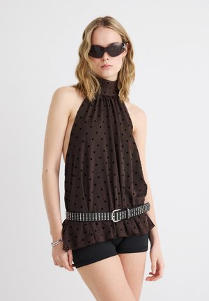 Kvinde iført sort ærmeløs top med prikker og nittebælte, sorte shorts, sølvarmbånd og store sorte solbriller.