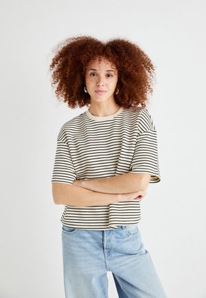 T-shirt a righe a maniche corte in crema e nero, con un taglio oversize e scollatura rotonda, abbinata a jeans azzurri chiari.