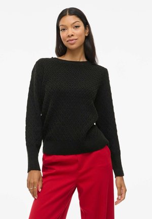 Pull en tricot noir avec motif en losange, manches larges, poignets et ourlet côtelés. Assorti avec un pantalon rouge. Texture lisse.