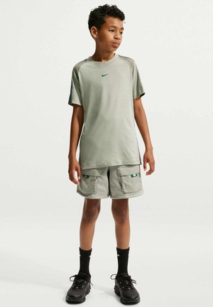Dreng stående iført en lysegrå Nike T-shirt, matchende cargoshorts, sorte sokker og sorte sneakers mod en ensfarvet lys baggrund.