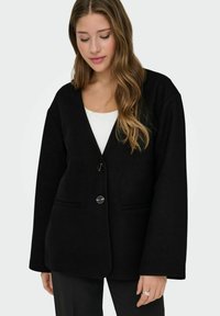 Blazer noir surdimensionné avec un col en V, deux poches avant et une fermeture à un bouton. Tissu texturé avec une finition lisse.