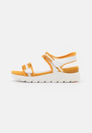 Sandale à bout ouvert avec lanières blanches et orange, fermetures réglables à Velcro, semelle intérieure rembourrée et semelle extérieure blanche épaisse à relief.