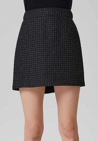 Jupe courte noire en tissu texturé avec un motif tissé. Elle présente une taille ajustée et une fente latérale pour un détail supplémentaire.