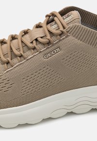 Sapatilha GEOX bege com um superior em malha, painel lateral texturizado, sistema de atacadores distinto e uma sola branca e almofadada.