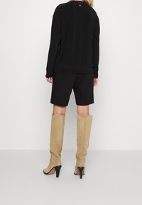 Svart, långärmad topp med lös passform och ribbad nederkant, matchad med svarta shorts. Bär beige mockastövlar med knähöjd och svarta klackar.