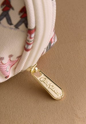 Prim-plan al unui săculeț din țesătură albă cu fermoar auriu gravat cu inscripția "Cath Kidston".