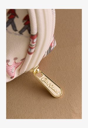 Prim-plan al unui săculeț din țesătură albă cu fermoar auriu gravat cu inscripția "Cath Kidston".