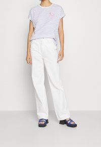 Camiseta a rayas en blanco y azul marino con un gráfico de flamenco; combinada con pantalones anchos blancos y sandalias azules de tiras con tacones gruesos.