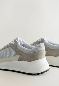 Chunky Sneakers mit einem Obermaterial aus grauem Wildleder und weißem Mesh, einer dicken weißen Sohle und einer schwarzen Gummisohle, geschnürt mit weißen Schnürsenkeln.