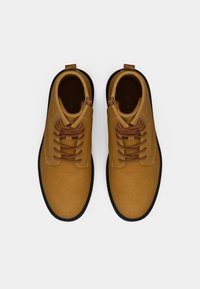Brązowe skórzane botki za kostkę z brązowymi sznurówkami, okrągłym noskiem i czarną gumową podeszwą. Posiadają pętelkę przy pięcie ułatwiającą zakładanie.