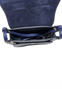 Mała, otwarta, ciemnoniebieska skórzana torebka z widocznymi wewnętrznymi przegródkami i zamykaną na zamek kieszenią pod złożonym zamszowym klapkiem.