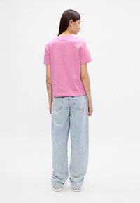 Rozā kokvilnas T-krekls ar īsām piedurknēm un noapaļotu kakla izgriezumu, saskaņots ar brīvām, gaiši zila denima biksēm. Redzama šuvju apdare un aizmugures dizains.