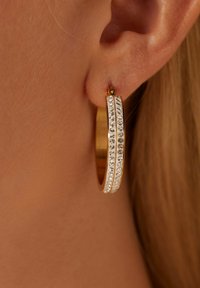 Gouden oorbellen in de vorm van hoops, met twee rijen heldere rhinestones langs de voorkant, een gladde, glanzende afwerking en een subtiel ontwerp.