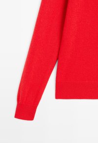 Czerwony sweter z długim rękawem, dzianinowy, z ribbowymi mankietami na tle białym.
