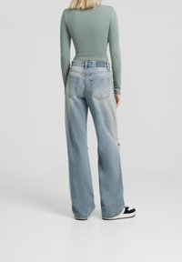 Light green long-sleeve top paired with high-waisted, wide-leg light blue denim jeans. Distressed details and classic back pockets visible.