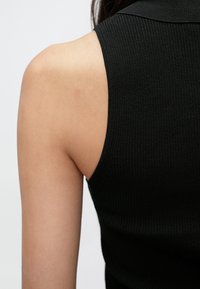 Crni bezrukavi top s rebrastim uzorkom, visokim izrezom i uskim krojem, koji ističe teksturu i glatki materijal.