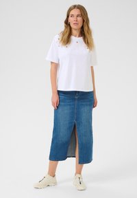 T-shirt en coton blanc avec des embellissements décoratifs, associé à une jupe en denim mi-longue avec une fente frontale et des baskets blanches décontractées.