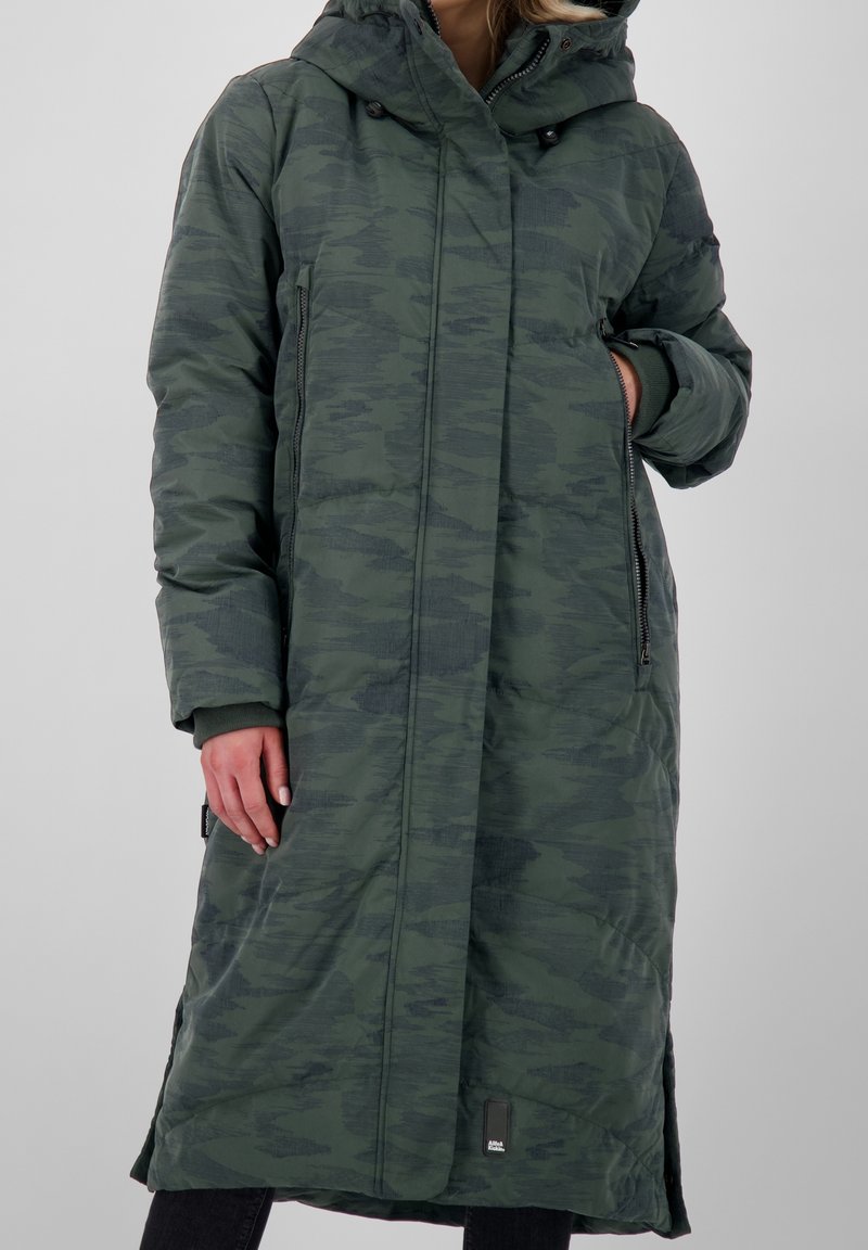 Lång, huva-kappa i mörkgrön kamouflage-mönster. Har dragkedjefickor på sidorna och ribbade muddar. Tillverkad av ett texturerat, syntetiskt material.