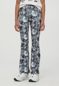 Leggings a fantasia nera e grigia con una texture liscia, caratterizzati da un design aderente che si allarga leggermente verso il fondo. Scarpe da ginnastica completano l'outfit.