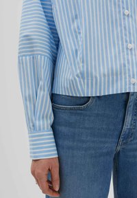 Hellblau-weiß gestreiftes Shirt mit einem kurzen Design, Knopfverschlüssen und langen Ärmeln, kombiniert mit blauen Jeans.