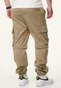 Khakifarbene Cargo-Hosen mit mehreren Taschen, elastischen Bündchen und einem glatten, leichten Stoff. Getragen mit weißen Sneakers, die schwarze Akzente zeigen.