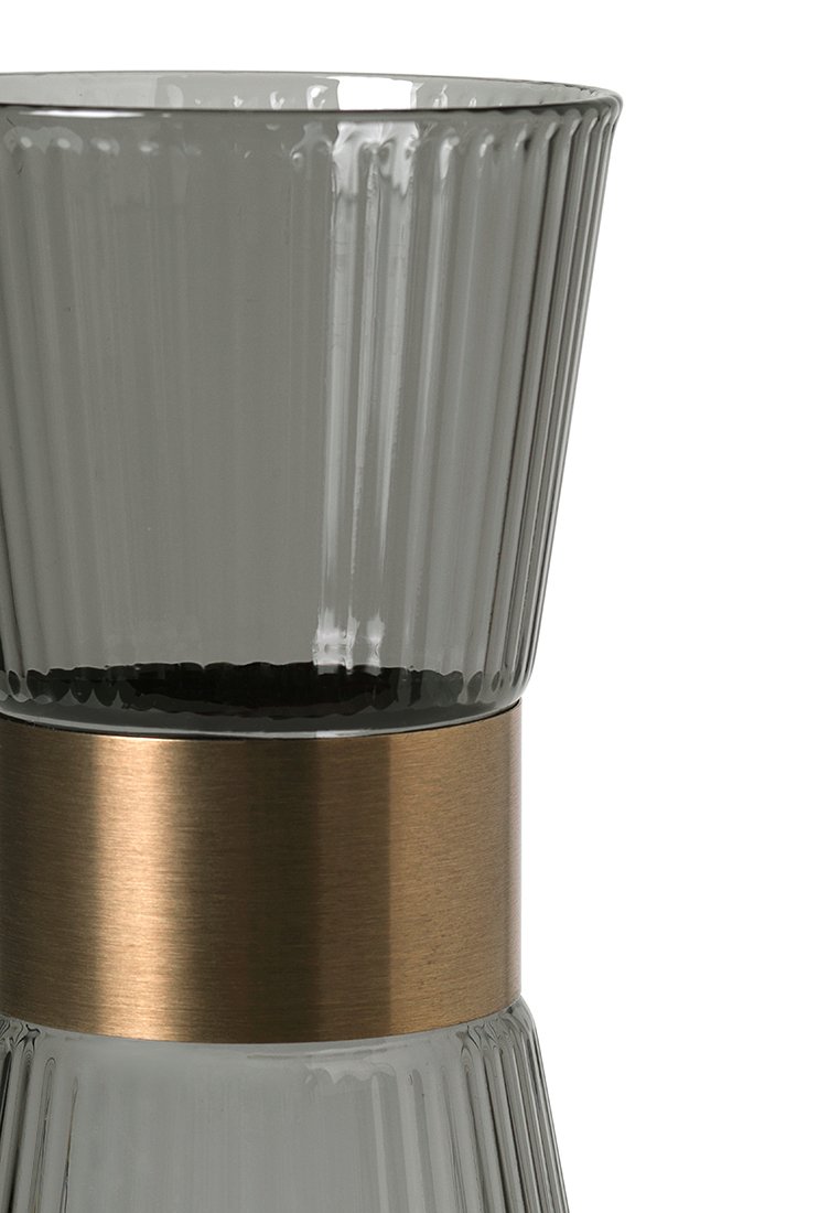 Jarrón de vidrio con un diseño estriado en gris y una banda metálica lisa de bronce alrededor de la parte media. La superficie texturizada refleja la luz.