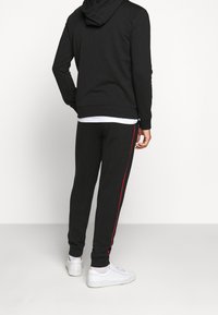 Svart hoodie med känguruficka och ärmslut, ihop med svarta joggers med röd sidosträng, kompletterad med vita sneakers.