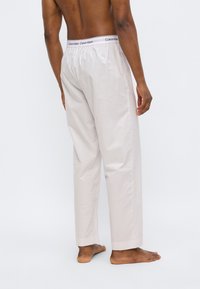 Φωτεινό μπεζ βαμβακερό παντελόνι πιτζάμας με ελαστική μέση που φέρει μαύρο λογότυπο, άνετη γραμμή, ίσια πόδια και χωρίς εμφανείς τσέπες.