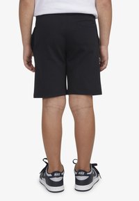 Fekete pamut rövidnadrág sima textúrával, oldal- és hátzsebbel, fekete-fehér tornacipővel viselve.