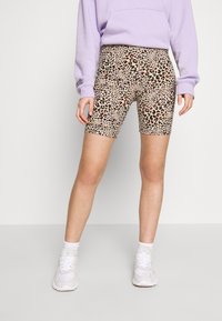 Shorts de vélo à imprimé léopard avec une base beige clair, présentant des taches vertes, orange et noires, associés à un sweat lavender et des baskets blanches.