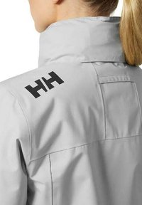 Light gray waterproof jacket with a high collar. Features a prominent black logo on the shoulder and a smooth, textured fabric.