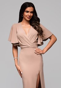 Sukienka w kolorze nude z falbanowymi rękawami, głębokim dekoltem w kształcie litery V i wysokim rozcięciem na udzie. Gładki materiał z dopasowanym krojem.