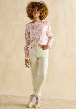 Langärmliges Oberteil mit rosa Blumenmuster, kombiniert mit elfenbeinfarbenen Jeans. Das Modell trägt hellviolette, gepunktete Socken und cremefarbene High-Heels.