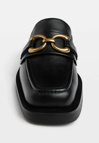 Mocassin en cuir noir à bout carré avec détail d’une boucle métallique double anneau dorée sur le dessus, sur fond blanc.