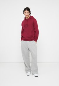 Bordoo kapuutsweater, millel on ees tasku ja logo, koos heledate hallide laia jala dressipükstega ja valgete jooksukingadega.