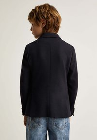 Blazer navy de tela texturizada con cuello de muesca, ajuste entallado y detalles de botones, combinado con jeans de mezclilla azul claro.