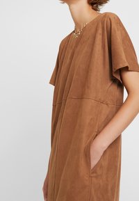 Braunes wildlederähnliches Kleid mit kurzen Ärmeln, einem runden Ausschnitt und Seitentaschen. Weicher Stoff mit minimalistischem Design für die Freizeit.