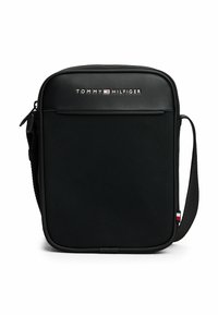 Bandolera negra con tejido texturizado, cierre de cremallera, bolsillo frontal y correa ajustable. Presenta el logo de Tommy Hilfiger y acentos de color.