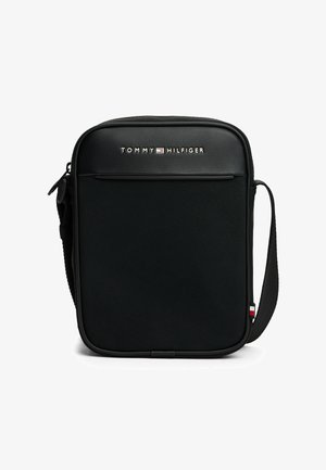 Czarna torba na ramię z teksturowanej tkaniny, z zamkiem błyskawicznym, przednią kieszenią i regulowanym paskiem. Posiada logo Tommy Hilfiger i kolorowe akcenty.