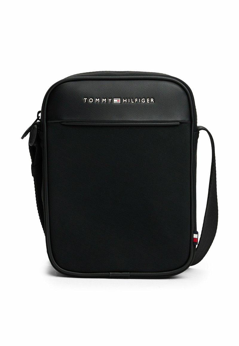 Bandolera negra con tejido texturizado, cierre de cremallera, bolsillo frontal y correa ajustable. Presenta el logo de Tommy Hilfiger y acentos de color.