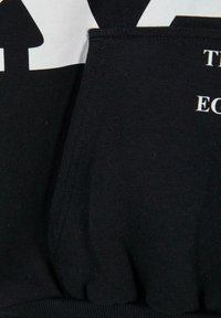 Gros plan d'un tissu noir avec un texte partiel blanc et un détail de couture froncée élastique.