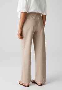 Beige wijde broek van een gestructureerde stof, met elastische tailleband en twee achterzakken. Vlotte, ademende materiaal.