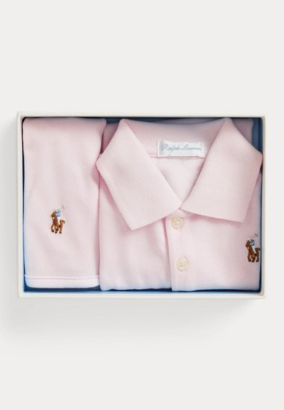Ανοιχτό ροζ polo Ralph Lauren και αντίστοιχο υφασμάτινο αντικείμενο σε άσπρο κουτί, και τα δύο με μικρά κεντημένα λογότυπα με άλογο και αναβάτη.
