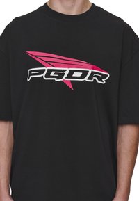 Black T-shirt featuring a pink and white logo with the text "PGDR." Short sleeves and a round neckline in a relaxed fit.