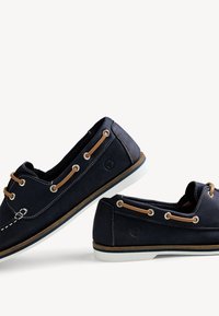 Paire de chaussures bateau bleu foncé avec semelles blanches et lacets beige, disposées côte à côte sur un fond blanc.