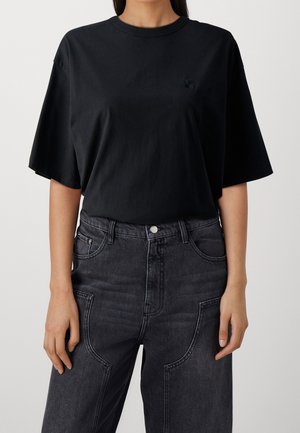 Kobieta nosząca luźny czarny t-shirt z krótkim rękawem włożony w wyblakłe czarne dżinsy z wysokim stanem i przednimi kieszeniami naszywanymi.