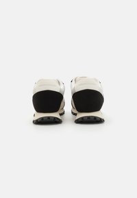 Sneakers featuring a black suede heel, white mesh upper, and rubber outsole with prominent treads. Minimalist design with logo detail.